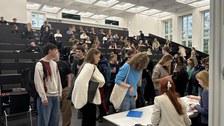 Studierende versammeln sich in einem Hörsaal der TU Dresden. Im Vordergrund melden sich einige Personen an einem Tisch bei zwei Mitarbeiterinnen an, während im Hintergrund viele weitere Studierende in den Sitzreihen Platz nehmen.