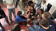 Studierende bauen gemeinsam einen Turm aus Spaghetti und Marshmellows. Einige sitzen, andere stehen und bauen aktiv mit.