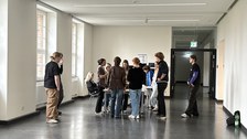 Studierende stehen gemeinsam in einem Flur eines Gebäudes um einen Tisch herum.