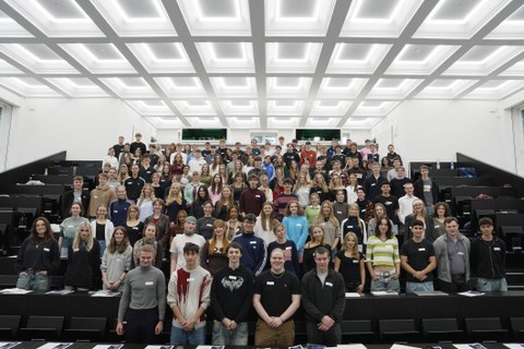 Many students are standing together in a large lecture hall for a group photo.