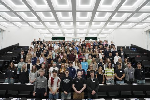 Many students are standing together in a large lecture hall for a group photo.