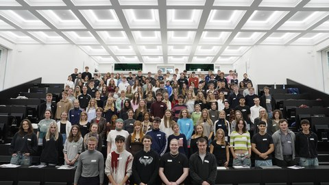 Viele Studierende stehen in einem großen Hörsaal für ein Gruppenbild zusammen.