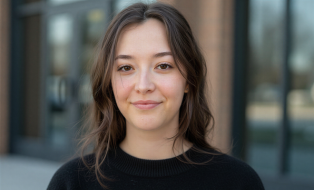 Frau mit braunen Haaren und schwarzen Pullover lächelt in Kamera