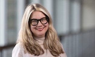 Frau mit langem blonden Haar und schwarzer runder Brille