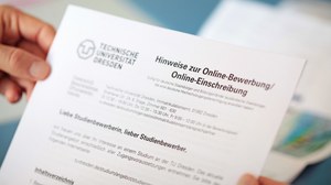 Foto von zwei Händen, die ein Dokument halten. Darauf ist neben einem Logo der TU Dresden zu lesen: "Hinweise zur online Bewerbung"