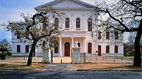 Universitätsgebäude der Stellenbosch-Universität. Weißes, schönes Haus mit Säulen und Bäumen davor. 