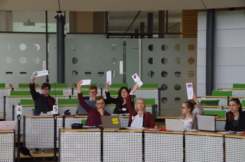 Studierende sitzen in einem Konferezsaal und halten Abstimmungskarten in die Höhe..