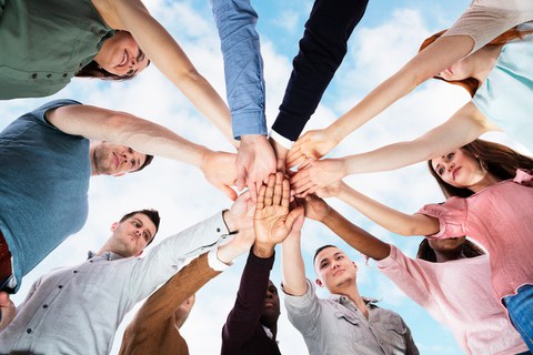 Foto: Zwölf im Kreis stehende Personen legen ihre Hände in der Mitte des Kreises übereinander.