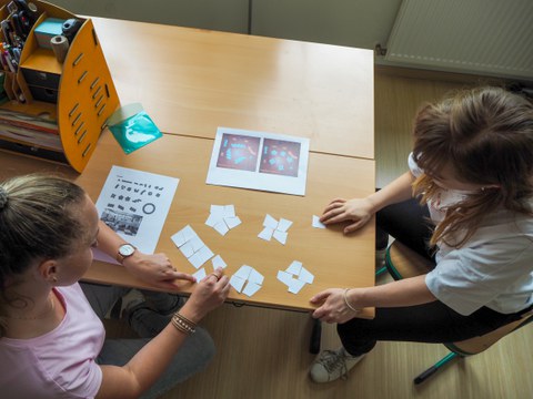 Zwei junge Frauen legen Papierkarten auf einen Tisch; Vogelperspektive