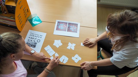 Zwei junge Frauen legen Papierkarten auf einen Tisch; Vogelperspektive