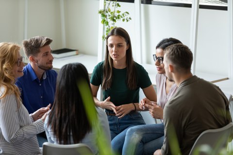 Foto: Sechs Personen sitzen sich in einem Kreis gegenüber und unterhalten sich.inem