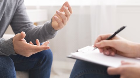 Foto zeigt einen Psychotherapeuten, der sich beim Gespräch mit einem Patienten Notizen macht.