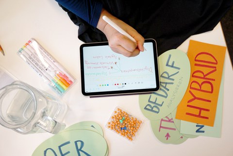 Foto einer Hand, die mit einem Stift auf einem Tablet Notizen aufschreibt.