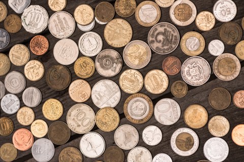 Das Foto zeigt Geldstücke aus verschiedenen Ländern und unterschiedlicher Währung. Sie liegen nebeneinander auf einem Holztisch.