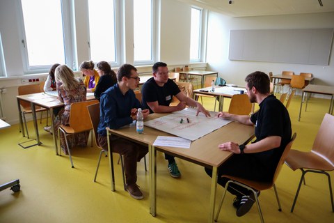 Das Bild zeigt Teilnehmende des Workshops "Gewalterfahrungen in der Rettungsdienstausbildung" diskutierend an einem Tisch in einem Seminarraum.