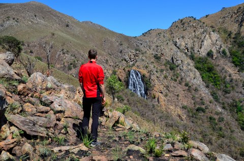 Bild eines Nationalparks in Eswatini. Im Vordergrund steht eine Person, die auf einen Wasserfall im Hintergrund schaut.