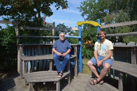 Foto: zwei Männer sitzen im Freien auf Holzbänken 