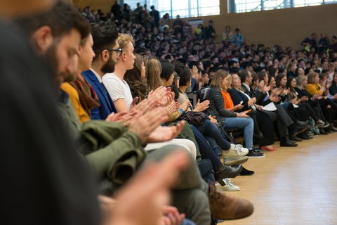 Foto eines großen Hörsaals, der voll belegt ist. Die sitzenden Personen klatschen.