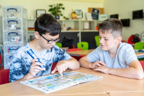 Das Foto zeigt zwei Jungen, die gemeinsam an einem Tisch sitzen und in einen Anybook-Reader gucken.  