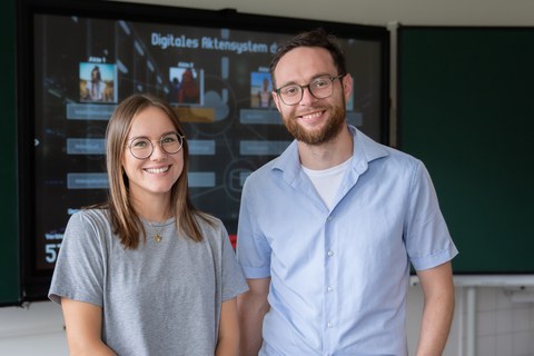 Mann und Frau stehen vor einer digitalen Schultafel.