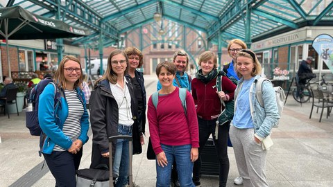 Gruppe von acht Frauen mit ihrem Gepäck. Im Hintergrund ist die Überdachung des Bahnhofsgebäudes zu sehen.