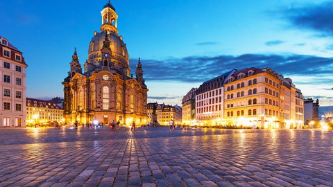 Foto des Dresdner Neumarktes mit der Frauenkirche. Es ist Abend, einige Menschen sind auf dem Neumarkt zu Fuß unterwegs.