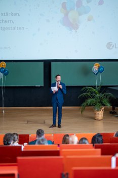 Mann hält Vortrag auf einer Bühne im Hörsaal