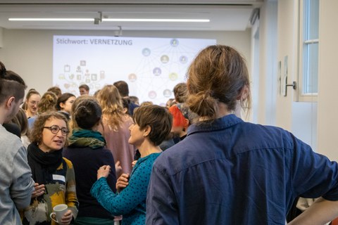 Das Foto zeigt einen jungen Mann von hinten, im Hintergrund herrscht buntes Treiben. 