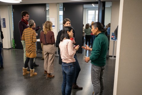 Eine Gruppe von 3 Personen unterhält sich. Im Hintergrund sind weitere Konversationen zu sehen.