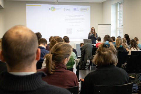 Foto zeigt einen Saal mit einer Frau, die einen Vortrag hält.