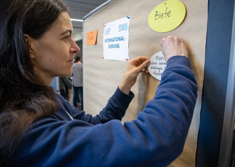 Eine Frau pinnt einen Zettel an eine Wand.