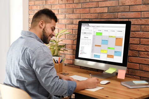 Junger Mann nutzt Kalender-App am Computer im Büro