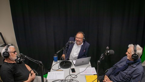 Drei Männer, die an einem Tisch sitzen und einen Podcast aufnehmen.
