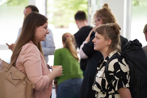 Zwei Frauen unterhalten sich miteinander. Im Hintergrund sind weitere Personen zu erkennen.