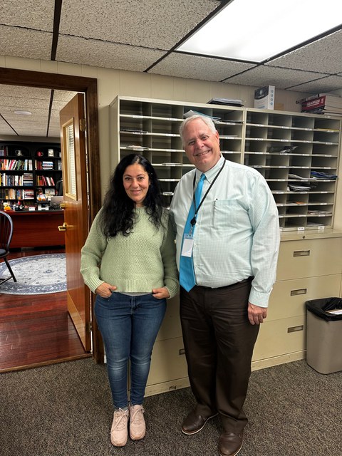 Frau und Mann stehen nebeneinander vor einer Regalwand in einer Schule