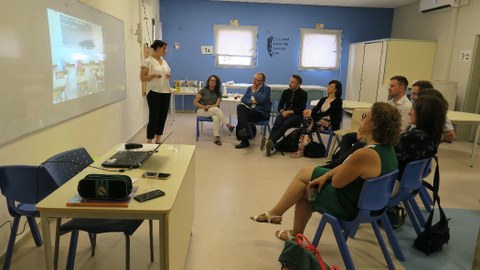 Bild von 10 Personen in einem Raum der israelischen Grundschule Nofei Yam. 9 Personen sitzen im Halbkreis und hören einer Frau zu, die vor einem Whiteboard steht, an dem eine Präsentation zu sehen ist.