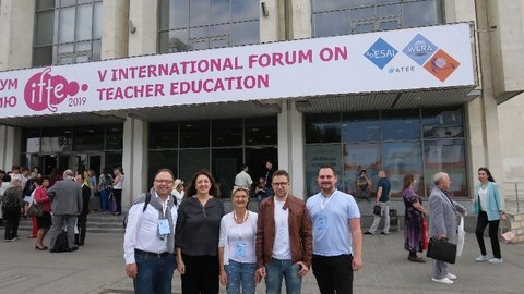 Gruppenbild von fünf Erwachsenen, die vor einem Gebäude der Universität Kazan stehen und in die Kamera lächeln. Im Hintergrund sind weitere Menschen zu sehen.