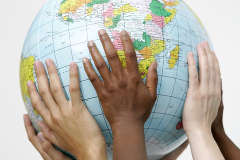 Bild von 6 Händen, die gemeinsam einen Globus hochhalten