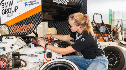 Foto einer jungen Frau, die in gehockter Haltung an einem Rennwagen arbeitet.