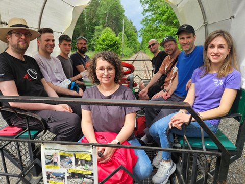 9 Personen sitzen auf einer Draisine und fahren auf Schienen