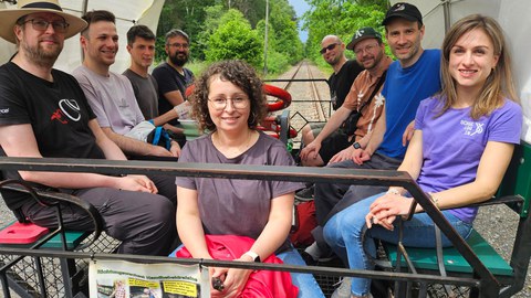 9 Personen sitzen auf einer Draisine und fahren auf Schienen