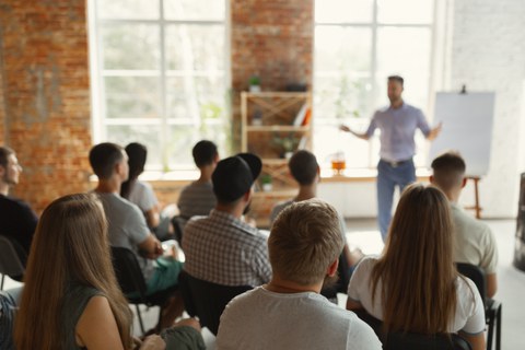 Männlicher Redner bei einem Vortrag in einem Universitäts-Workshop. Zuhörerschaft oder Konferenzsaal. Rückansicht von unerkannten Teilnehmern im Publikum.