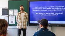 Ein Mann steht neben einer digitalen Tafel und hält einen Vortrag.