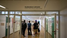 Eine Gruppe steht in einem Gang eines Unigebäudes. Über der Durchgangstür steht "Studienbüro Lehramt"