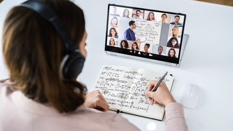 Das Foto zeigt eine Person, die Notizen in ein Heft schreibt, während sie auf ein Tablet schaut. 