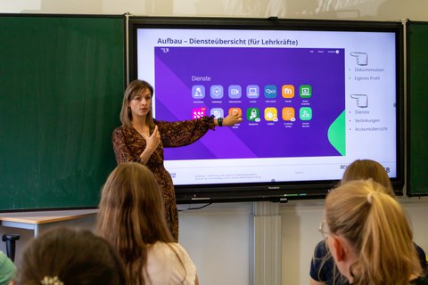 Frau hält Vortrag und steht vor einer digitalen Tafel