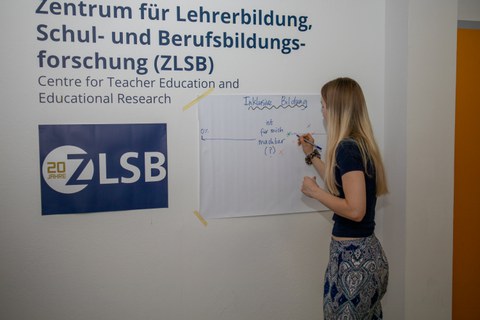 Frau schreibt etwas auf einem Flipchartpapier, welches an einer Wand hängt.