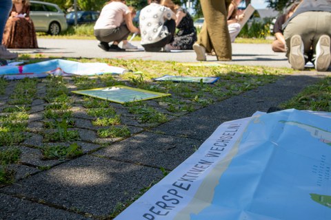 Zu sehen ist eine Landkarte im Vordergrund, im Hintergrund arbeiten junge Menschen kollaborativ am Boden