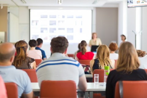 Das Bild zeigt eine Gruppe von Zuhörern in einem Seminarraum während einer Präsentation.