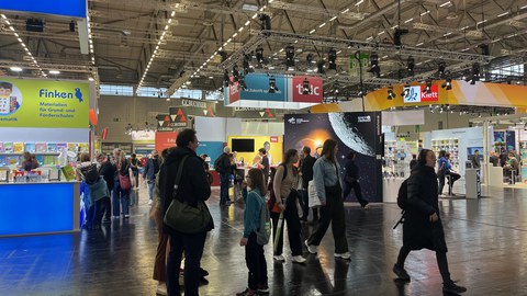 Zu sehen ist eine Messehalle, wo buntes Treiben herrscht